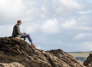 DI Humphrey Goodman sitzt auf einem Felsen an der Küste und sieht nachdenklich aus